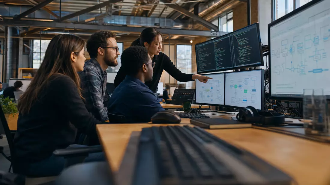 Software-Team bespricht Prozessdiagramme in industriellem Büro mit mehreren Monitoren
