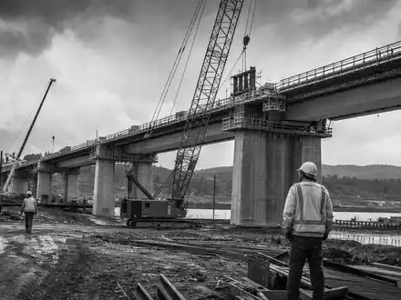 Dokumentarisches Schwarzweiß-Reportagefoto einer großen Brückenbaustelle symbolisiert Ferrovial SE, ISIN NL0015001IX2, als internationalen Baukonzern der Branche - Foto: THN