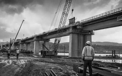 Dokumentarisches Schwarzweiß-Reportagefoto einer großen Brückenbaustelle symbolisiert Ferrovial SE, ISIN NL0015001IX2, als internationalen Baukonzern der Branche - Foto: THN
