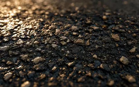 Detaillierte Makroaufnahme von nassem Asphalt zeigt Baumaterial-Textur und steht für Ferrovial SE, ISIN NL0015001IX2, Baukonzern - Foto: THN