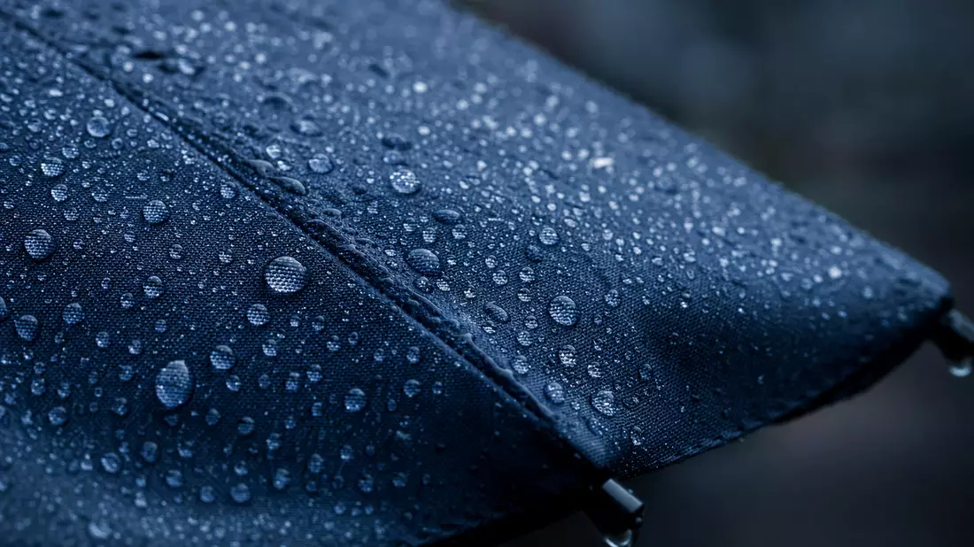 Makroaufnahme von Regentropfen auf dunkelblauem Regenschirmstoff mit weichem Licht