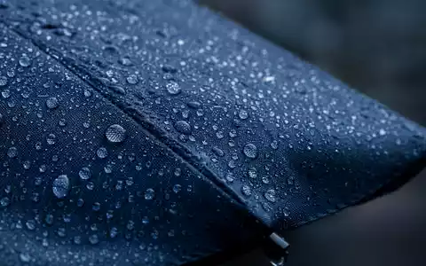 Aviva plc (ISIN GB0002162385) fokussiert Makroaufnahme von Regentropfen auf dunklem Regenschirmstoff symbolisch - Foto: THN