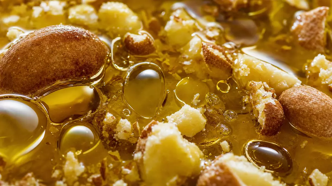 Extreme Nahaufnahme von goldenem Pflanzenöl und Nussfragmenten mit glänzender Textur