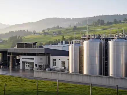 Fotorealistische Aufnahme einer Molkereianlage zeigt die Branche von Emmi AG, ISIN CH0012829898, in Schweizer Landschaft - Foto: THN