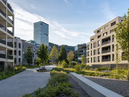 Allreal Holding AG (CH0008837566) zeigt fotorealistisch moderne Schweizer Wohnüberbauung mit Grünanlagen und Hochhaus im Hintergrund - Foto: THN