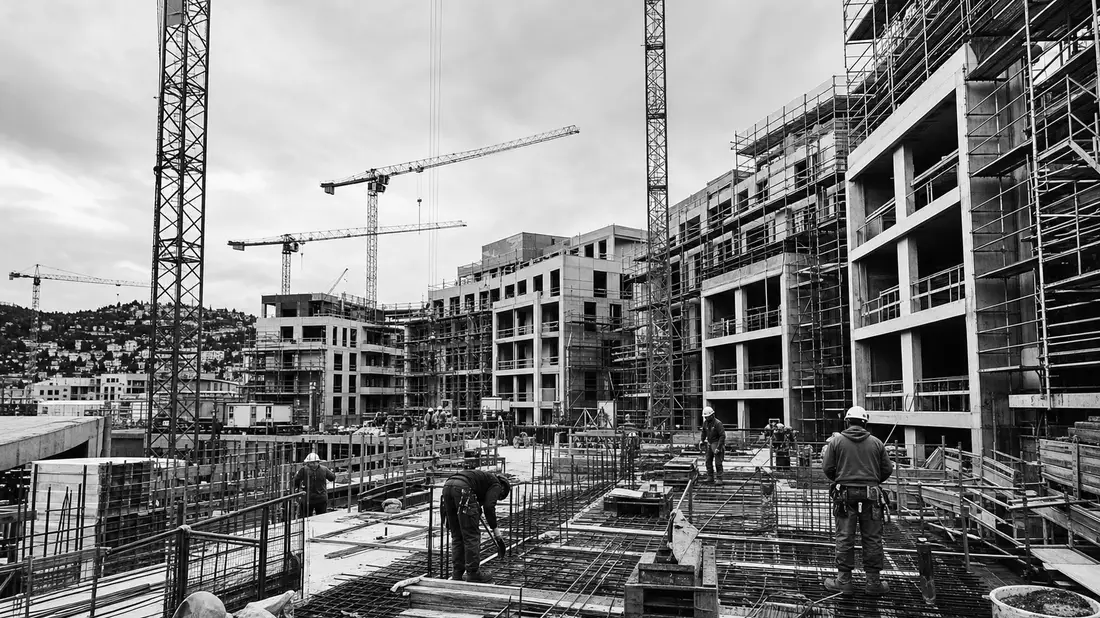 Schwarzweiß-Reportagefoto einer Baustelle mit Kränen und Bauarbeitern