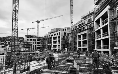 Allreal Holding AG (CH0008837566) dokumentiert in Schwarzweiß eine Baustelle mit Kränen und Bauarbeitern - Foto: THN