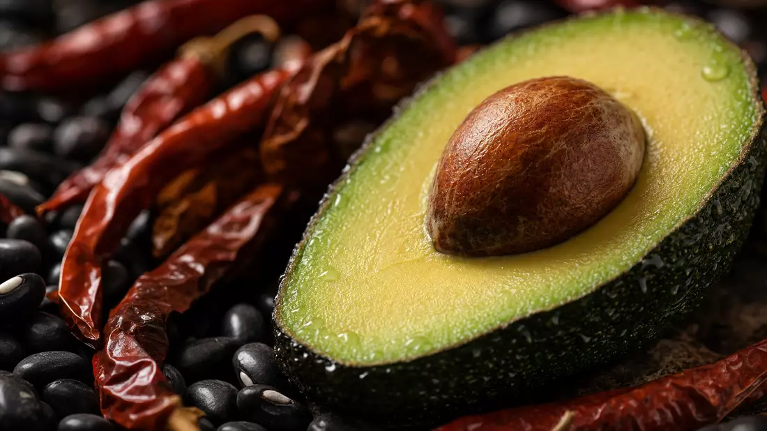 Extreme Makro-Nahaufnahme einer halbierten reifen Avocado mit Chili-Peppers und schwarzen Bohnen