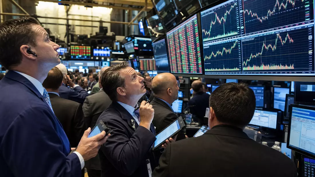 Trader auf dem Börsenparkett betrachten Kursdiagramme auf großen Bildschirmen der Börse