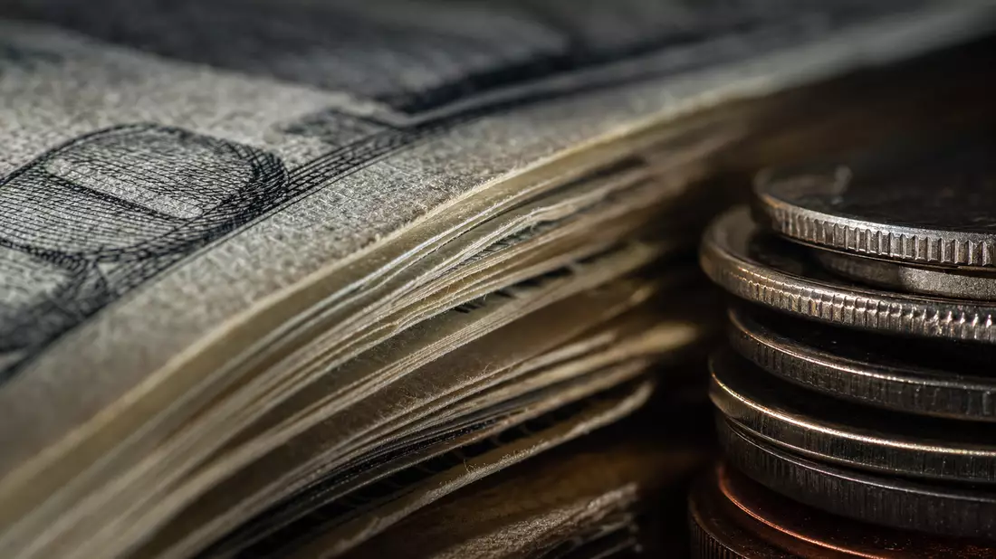Makroaufnahme von gestapelten Dollarnoten und glänzenden Münzen im dramatischen Licht