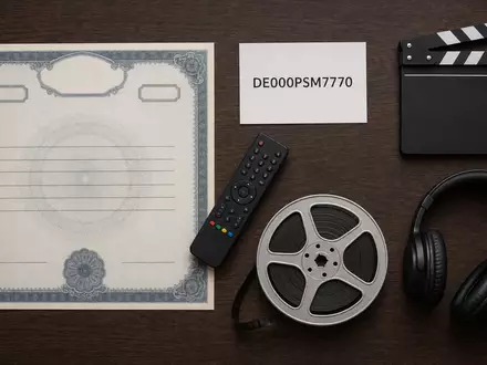 ProSiebenSat.1 Media DE000PSM7770 zeigt ein Flatlay mit Aktienzertifikat, ISIN-Karte, Fernbedienung und Filmutensilien auf Holztisch - Foto: THN