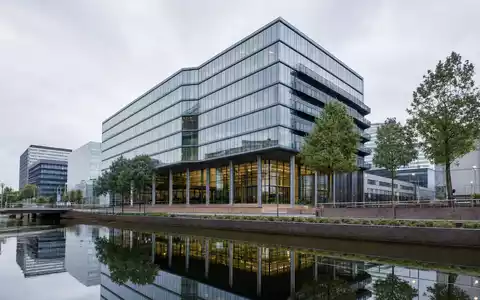 Fotorealistisches Amsterdamer Bürogebäude symbolisiert Prosus N.V., ISIN NL0013654783, moderne Beteiligungsholding am Kanal - Foto: THN