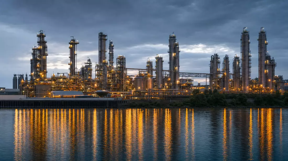 Chemieanlage mit beleuchteten Destillationstürmen am Wasser in der Abenddämmerung