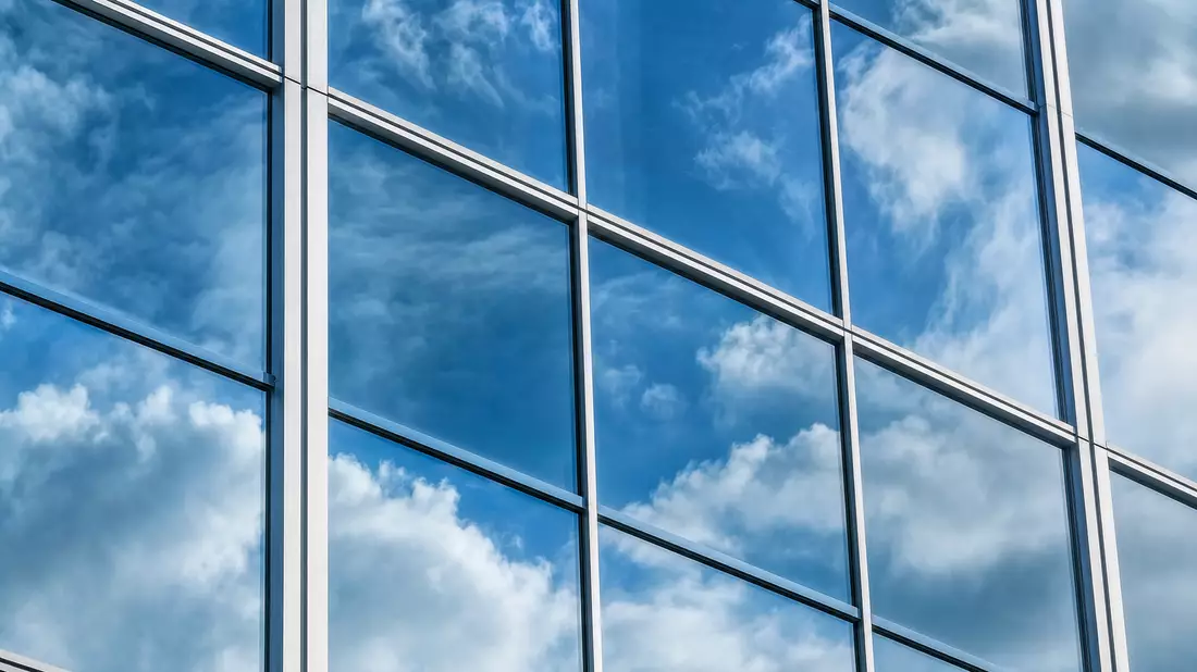 Extreme Nahaufnahme einer Glasfassade mit spiegelnden Wolken und geometrischem Fensterraster