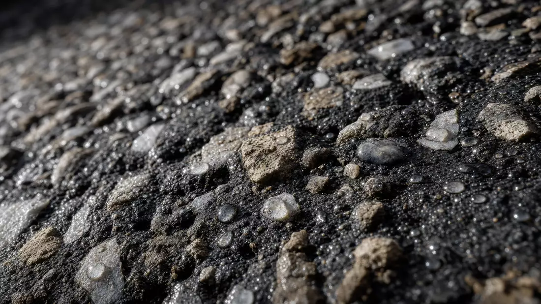 Extreme Makroaufnahme von nassem Asphalt und Betonkies mit glänzenden Wassertropfen