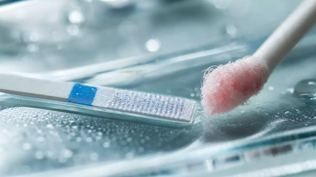 Makrofoto eines Diagnostik-Teststreifens und Wattestäbchens mit Tröpfchen auf Glasoberfläche