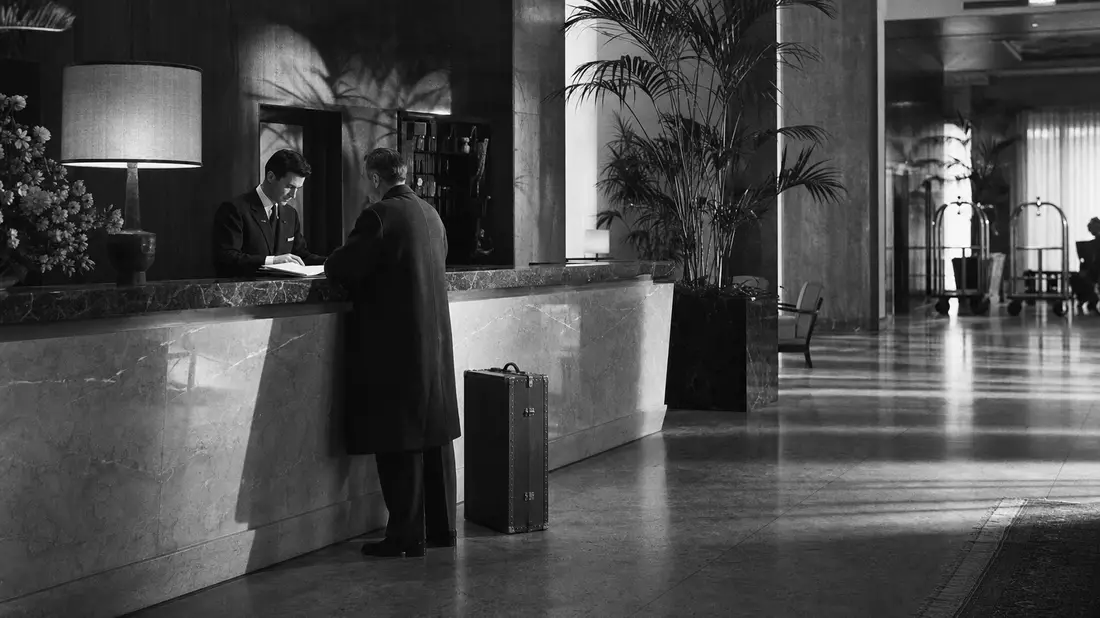 Schwarzweiß-Reportage: Concierge und Gast an Marmorrezeption im Hotellobby, Host Hotels & Resorts
