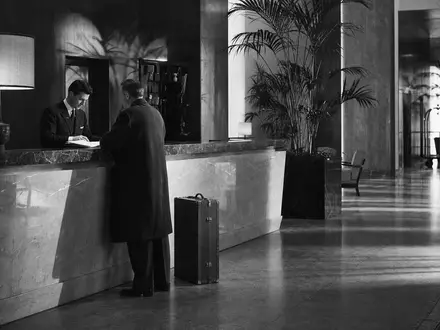 Host Hotels & Resorts US44107P1049 – dokumentarische Schwarzweiß-Reportage mit Gast und Concierge an klassischem Hotelempfang - Foto: THN