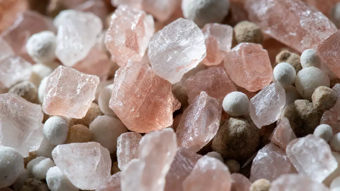 Extreme Makroaufnahme von rosa Kristallen und weißem Düngemittel-Granulat mit Lichtreflexen