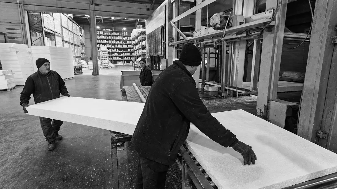 Schwarzweiß-Dokumentarfoto von Arbeitern mit Dämmplatten in Fabrikhalle