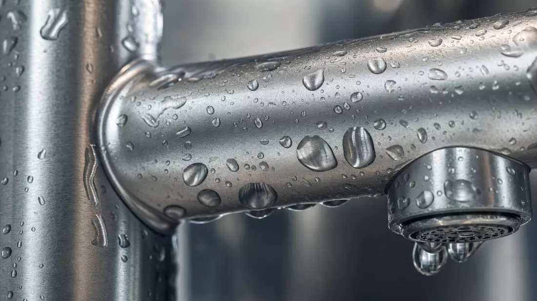 Extreme Nahaufnahme einer Chromarmatur mit glänzenden Wassertropfen