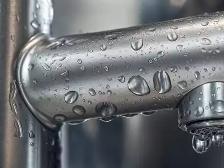 Masco Corporation US5745991068 zeigt eine detaillierte Makroaufnahme einer gebürsteten Metallarmatur mit glänzenden Wassertropfen - Foto: THN