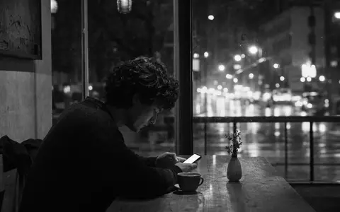 Match Group Inc. (ISIN US57669L1008) illustriert Schwarzweiß-Reportage einer Person mit Smartphone in nächtlichem Café - Foto: THN