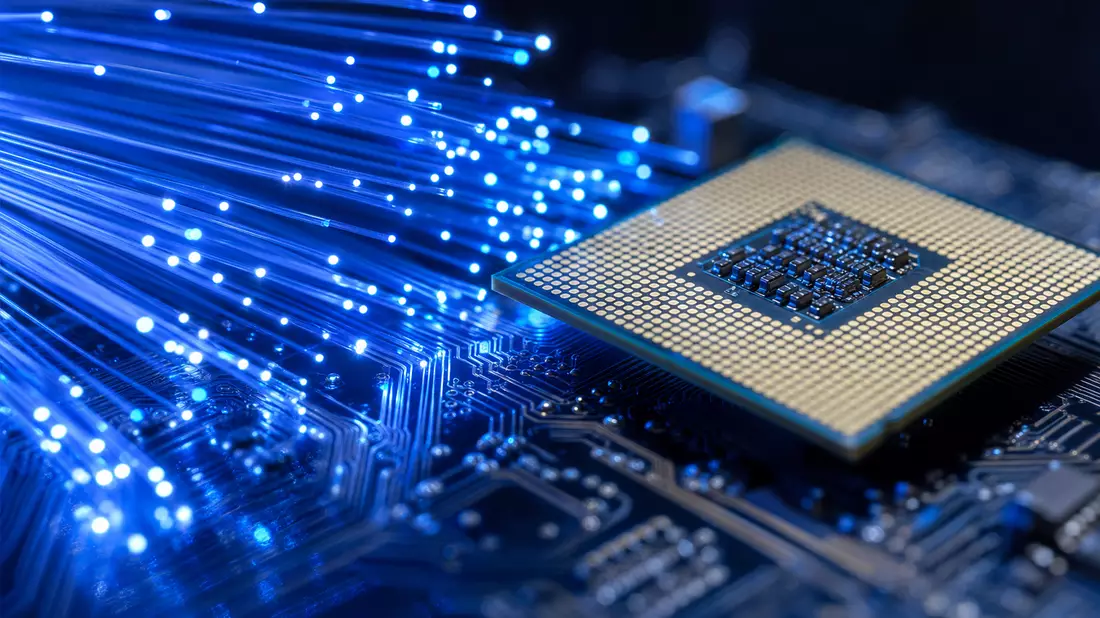 Makroaufnahme leuchtender Glasfaserstränge neben einem Prozessorchip mit Leiterbahnen