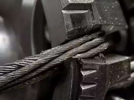 Otis Worldwide Corp. (US68902V1070): Makroaufnahme eines Stahlseils verflochten mit einem metallischen Getriebezahn - Foto: THN