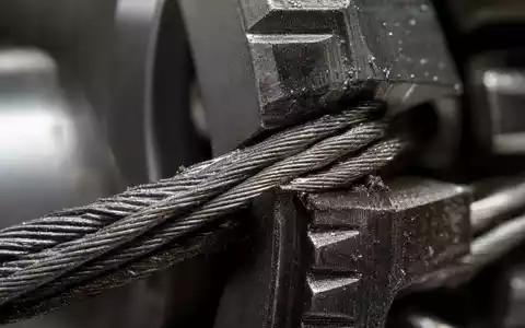 Otis Worldwide Corp. (US68902V1070): Makroaufnahme eines Stahlseils verflochten mit einem metallischen Getriebezahn - Foto: THN