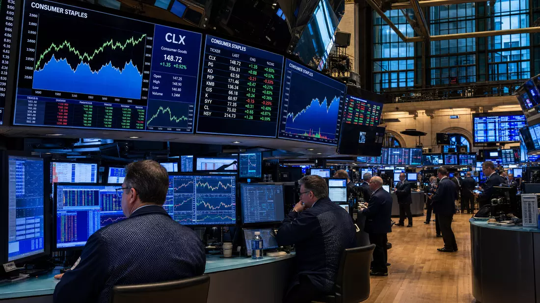 NYSE-Börsenparkett mit Händlern und digitalen Anzeigetafeln für Konsumgüter-Aktien