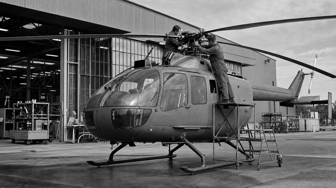 Schwarzweiß-Dokumentaraufnahme von Technikern an einem Helikopter in Werkshalle