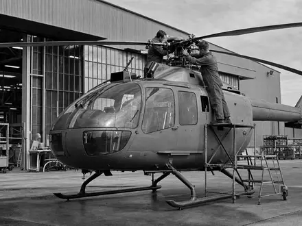 Schwarzweiß-Reportagefoto zeigt Techniker an unmarkiertem Helikopter, dokumentarischer Stil für Textron Inc. (US8832031027) Luftfahrtsektor - Foto: THN