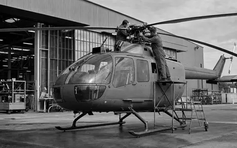 Schwarzweiß-Reportagefoto zeigt Techniker an unmarkiertem Helikopter, dokumentarischer Stil für Textron Inc. (US8832031027) Luftfahrtsektor - Foto: THN