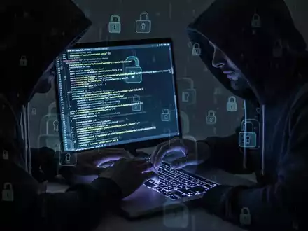 Verschattete Gestalt in Kapuzenjacke tippt auf Laptop, Code-Zeilen und digitale Schloss-Symbole auf dem Bildschirm. - Foto: über boerse-global.de