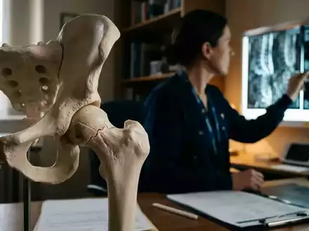 Nahaufnahme eines menschlichen Hüftgelenkmodells mit Knochenschäden vor einem unscharfen Hintergrund eines Arztes, der medizinische Scans betrachtet. - Foto: über boerse-global.de