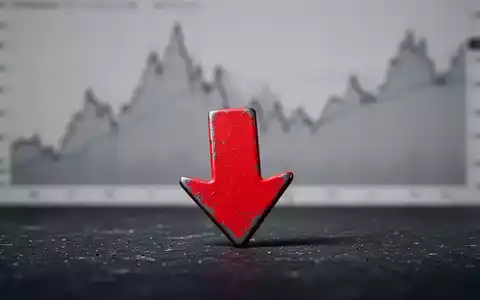 Ein roter Abwärtspfeil, der fast eine dunkle Oberfläche berührt, mit einem verschwommenen Finanzchart im Hintergrund. - Foto: über boerse-global.de