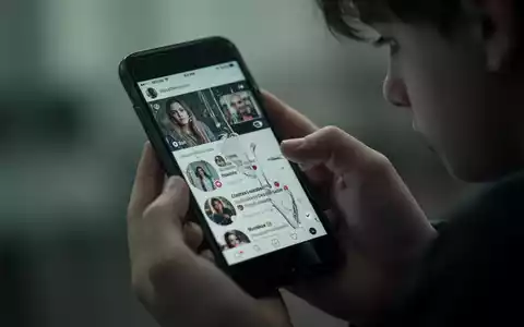 Eine Nahaufnahme einer jugendlichen Hand, die ängstlich ein Smartphone umklammert, dessen Bildschirm einen verzerrten Social-Media-Feed widerspiegelt. - Foto: über boerse-global.de
