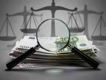 Ein stilisiertes Bild eines Vergrößerungsglases über einem Stapel Euro-Banknoten, mit Schatten von Waagen der Gerechtigkeit im Hintergrund. - Foto: über boerse-global.de