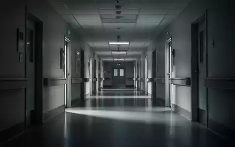 Ein langer, leerer und etwas düsterer Krankenhausflur mit glänzenden Böden und sanften Schatten, der Herausforderungen im Gesundheitswesen symbolisiert. - Foto: über boerse-global.de