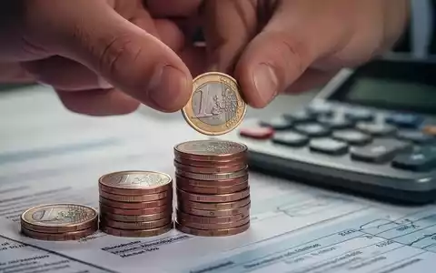 Eine Hand legt Münzen auf einen Stapel, mit unscharfen Finanzdokumenten im Hintergrund, symbolisiert steigende Krankenkassenbeiträge. - Foto: über boerse-global.de