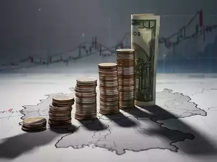 Ein stilisierter Stapel Münzen oder Geldscheine, der einen langen Schatten über eine Umrisskarte von Nordrhein-Westfalen wirft. - Foto: über boerse-global.de