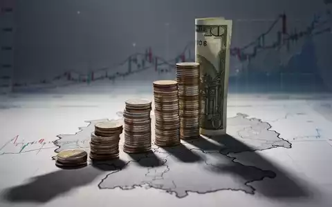 Ein stilisierter Stapel Münzen oder Geldscheine, der einen langen Schatten über eine Umrisskarte von Nordrhein-Westfalen wirft. - Foto: über boerse-global.de