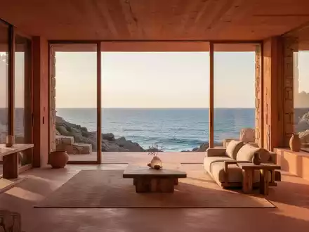 Ein minimalistisches Küstenhaus bei Sonnenuntergang, mit großen Fenstern, die den Blick auf das Meer freigeben und warme Erdtöne aufweisen. - Foto: über boerse-global.de
