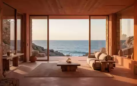 Ein minimalistisches Küstenhaus bei Sonnenuntergang, mit großen Fenstern, die den Blick auf das Meer freigeben und warme Erdtöne aufweisen. - Foto: über boerse-global.de
