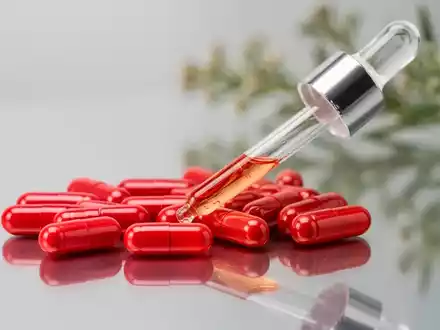 Nahaufnahme von leuchtend roten Astaxanthin-Kapseln und einer Tropfflasche auf einer reflektierenden Oberfläche mit botanischem Hintergrund. - Foto: über boerse-global.de
