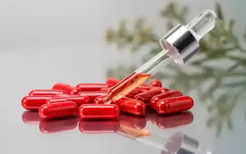 Nahaufnahme von leuchtend roten Astaxanthin-Kapseln und einer Tropfflasche auf einer reflektierenden Oberfläche mit botanischem Hintergrund. - Foto: über boerse-global.de