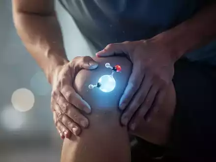 Eine Person hält sich schmerzgeplagt das Knie, während eine ruhige, blaue Lichtquelle auf Melatonin als Schmerzmittel hinweist. - Foto: über boerse-global.de