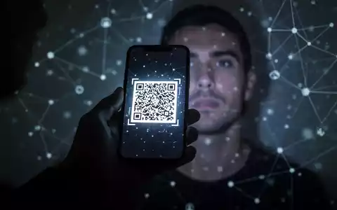 Eine Hand hält ein Smartphone mit einem bösartigen QR-Code, der auf ein unscharfes Gesicht projiziert wird, symbolisch für digitale Betrugsgefahren. - Foto: über boerse-global.de