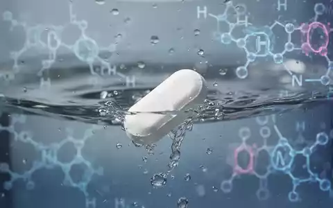 Eine weiße Pille löst sich in Wasser auf, im Hintergrund angedeutete wissenschaftliche Darstellungen von Hormonen und Stoffwechselwegen. - Foto: über boerse-global.de